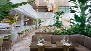 A modern restaurant with a bar area, seating with tables and booths, and abundant indoor plants. - Miami Luxury Executive Apartment (Miami)