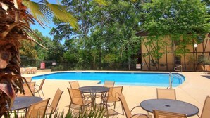 A swimming pool with lounge chairs and tables, surrounded by trees and a building. - CW B201 Comal Riverbahn Retreat B201 (New Braunfels)