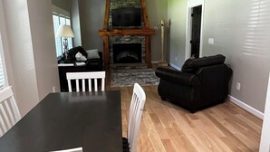 Een ruime woonkamer met een stenen open haard, houten plafond en een eettafel met stoelen.