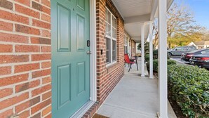 A brick building with a green door, a covered porch, and a red chair outside. - Cheerful Abode (Raleigh)