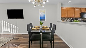A modern dining area with a rectangular table, black upholstered chairs, and a chandelier. - Cheerful Abode (Raleigh)