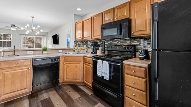 A modern kitchen with wooden cabinets, a black refrigerator, a microwave, a stove, and a dishwasher. - Cheerful Abode (Raleigh)