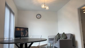 Un saló modern amb una taula de dinar rodona, un sofà amb coixins, una televisió i un rellotge de paret.