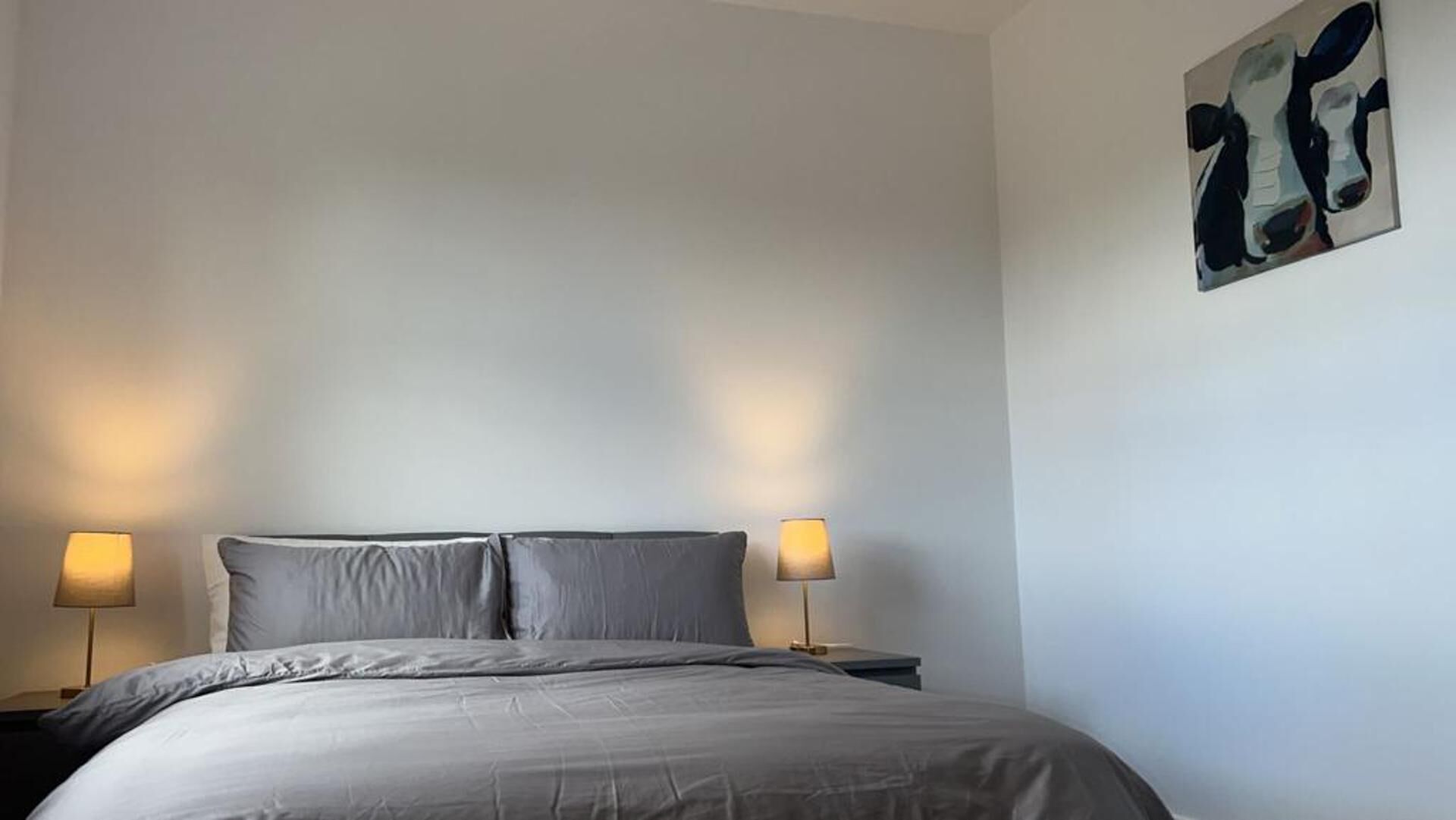 A bedroom with a bed, two bedside lamps, and a wall art piece.