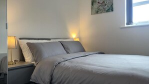 Un lit bien fait, avec une couette et des oreillers gris, une lampe de chevet et un tableau accroché au mur.