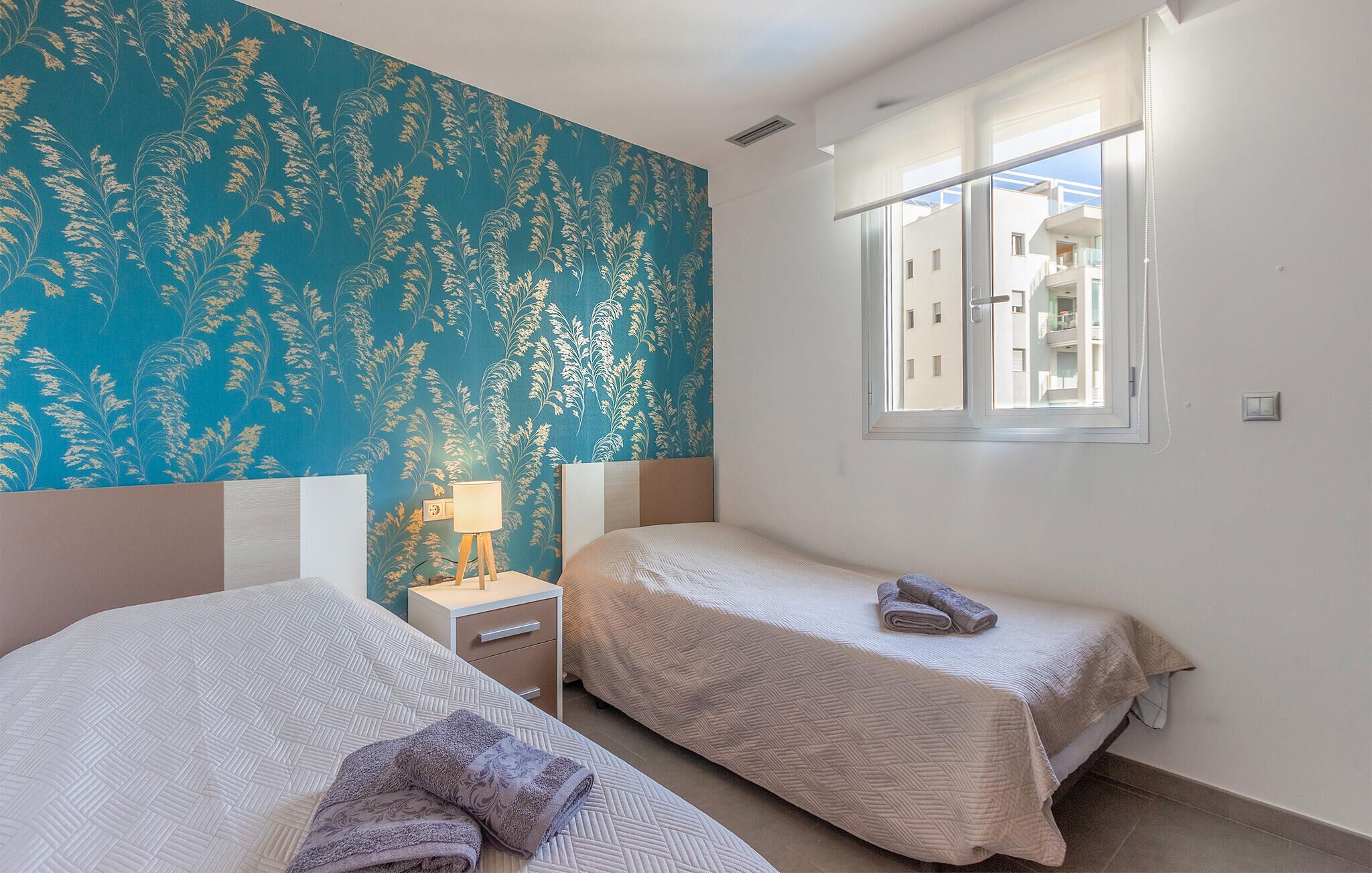 A room with two beds, a window, and a wall with a floral pattern.