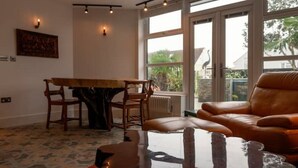 A room with a dining table, chairs, a leather sofa, and a large window with a view of greenery.