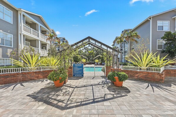 A gated pool area with a sign detailing pool rules, surrounded by brick walls and potted plants.
