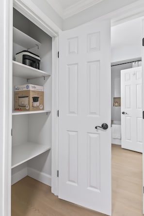 Una puerta blanca con manija que da a una habitación con piso de madera y pared blanca.