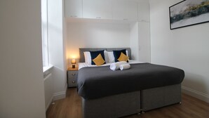 Een moderne slaapkamer met een groot bed, nachtkastje, lamp en een schilderij aan de muur.