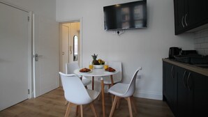 Een compacte keuken met een eettafel, witte stoelen, een flatscreen televisie boven het aanrecht en een klein ontbijt.