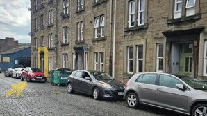 Een rij geparkeerde auto's langs een geplaveide straat, voor een rij bakstenen gebouwen met meerdere ramen en deuren.