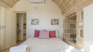 Ein Schlafzimmer mit einem großen Bett, weißer Bettwäsche, einer Steinwand und Blick auf ein Steinhaus.