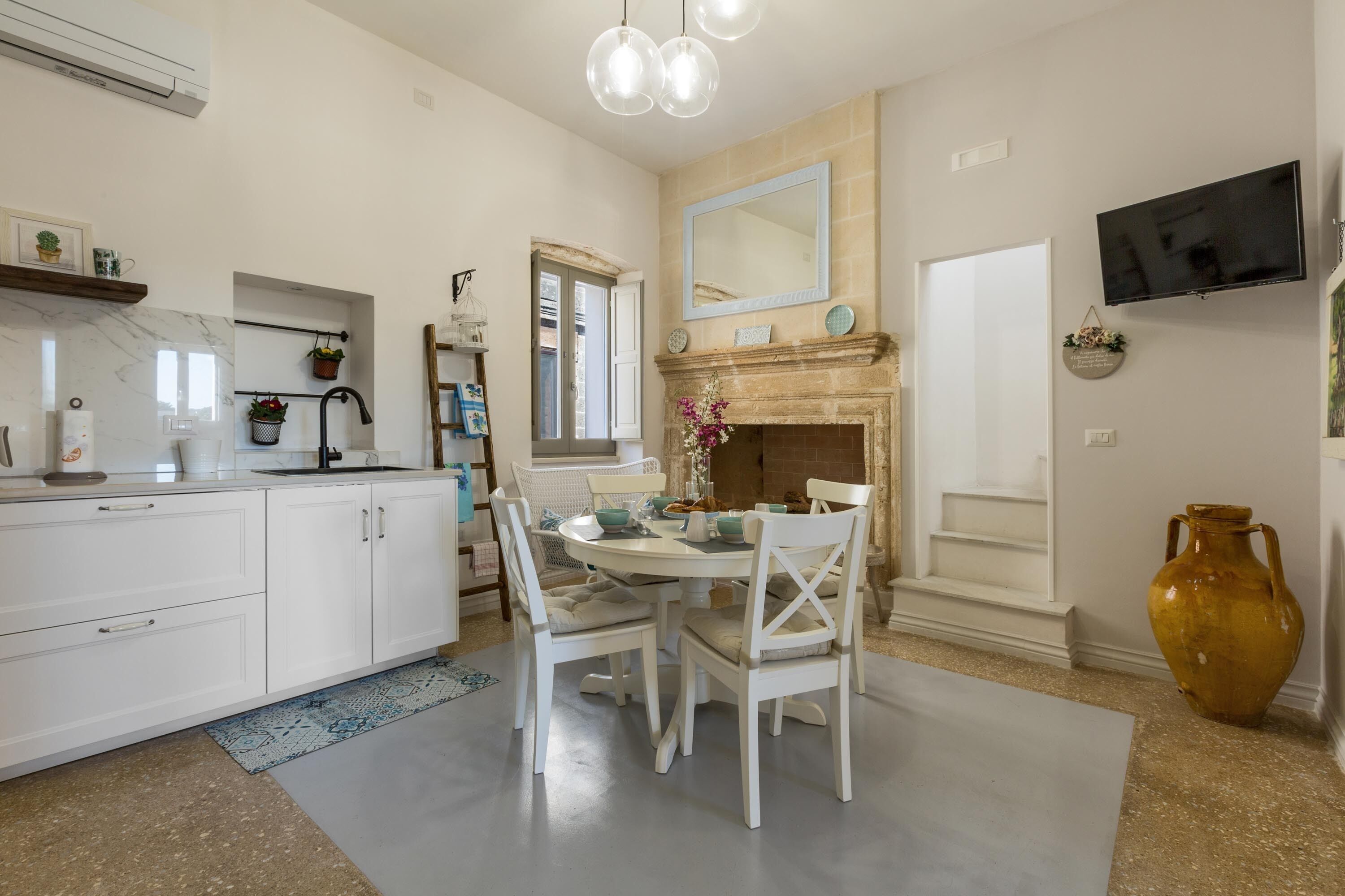 A modern kitchen with white cabinetry, a dining table with chairs, a fireplace, and a TV mounted on the wall.