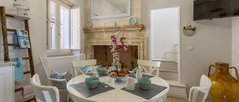 A dining area with a round table, white chairs, teal bowls, and a vase with flowers.