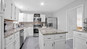 A modern kitchen with white cabinetry, granite countertops, stainless steel appliances, and a backsplash. - Pet-Friendly Tulsa Vacation Rental w/ Sunroom (Tulsa)