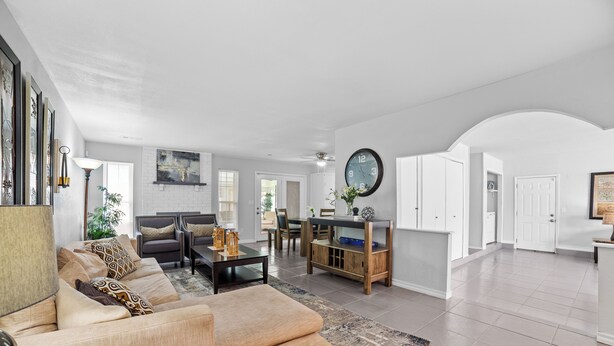 A spacious living room with a beige sofa, a coffee table, and a dining area with a wooden table and chairs. There is a clock on the wall and a door leading to another room. - Pet-Friendly Tulsa Vacation Rental w/ Sunroom (Tulsa)