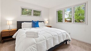 A bedroom with a bed, two bedside tables, a window, and a view of trees.