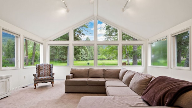 A room with a large sectional sofa, a patterned armchair, and a view of a green landscape through large windows.