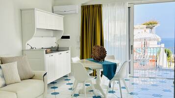 Une cuisine moderne avec des meubles blancs, un coin repas comprenant une table et des chaises, et un balcon avec vue sur la mer.