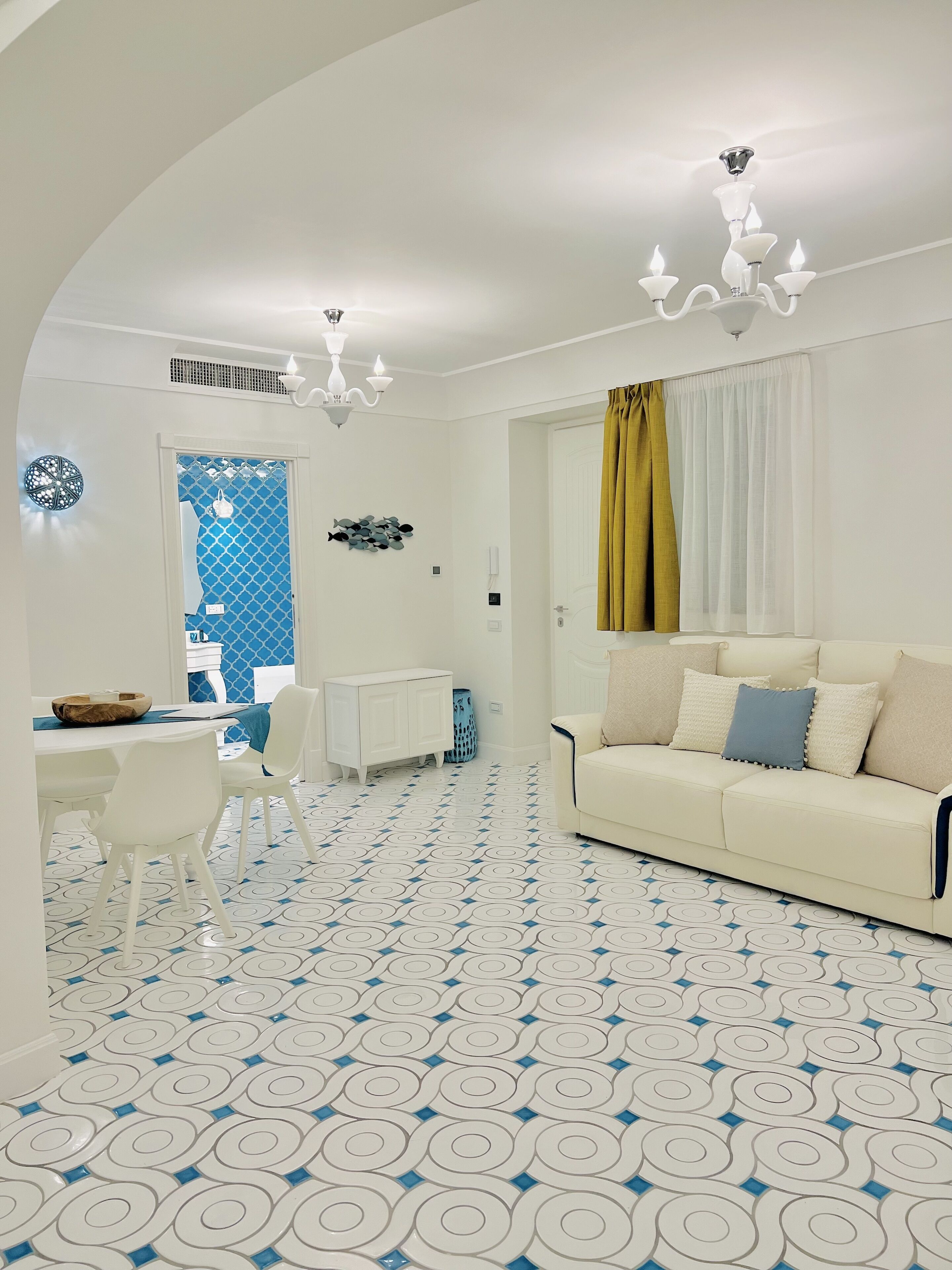 A modern living room with a white sofa, a dining area with a white table and chairs, and a patterned floor.