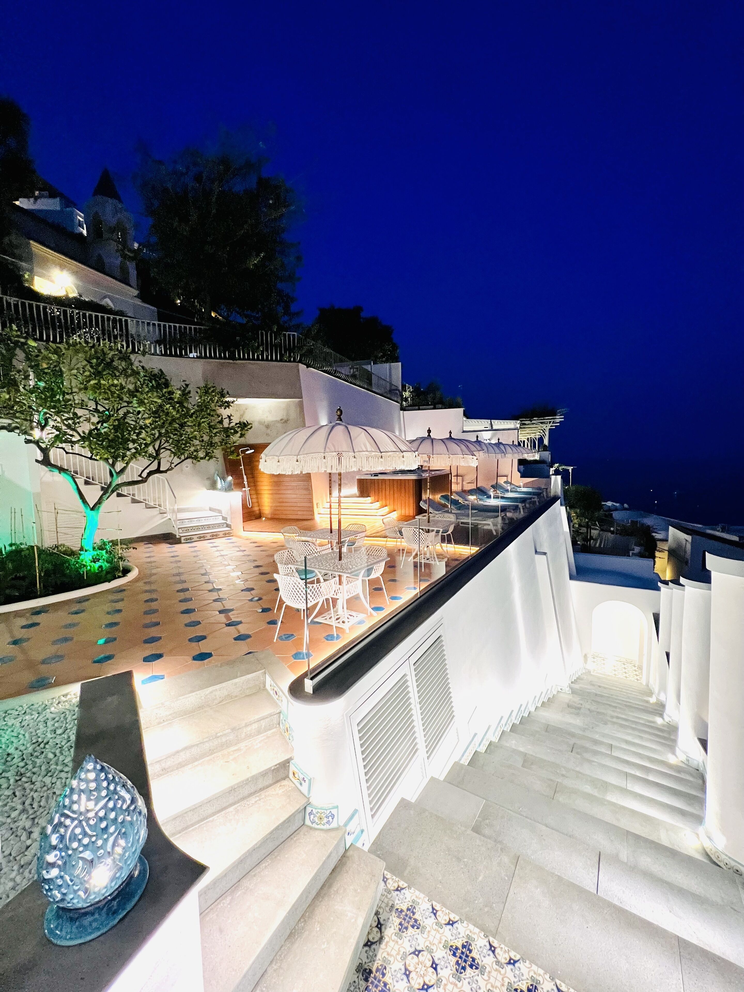 A terrace with outdoor seating, a staircase, and a view of the sea at dusk.