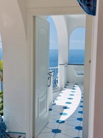 Una puerta que da a un balcón con suelo de baldosas y vista al mar.