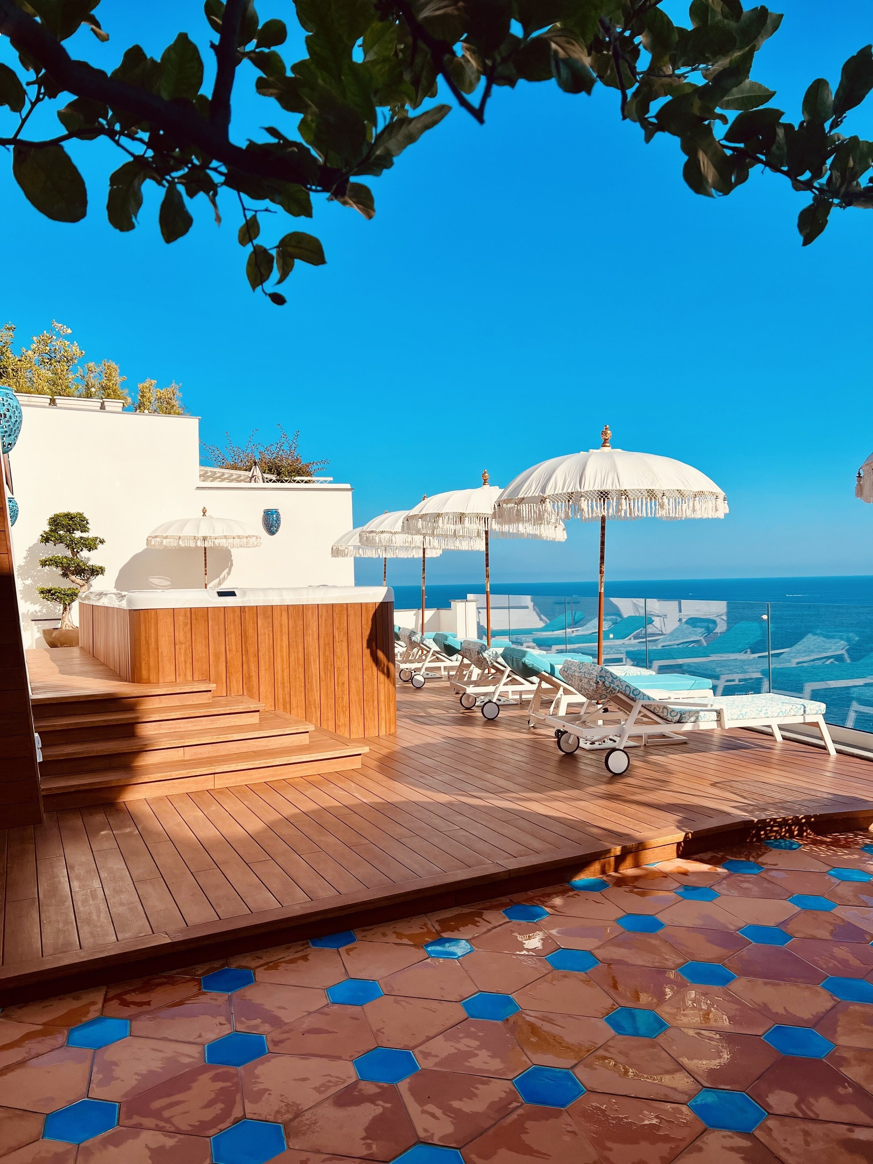 A wooden deck with hexagonal tiles, lounge chairs, and white umbrellas overlooking a body of water.