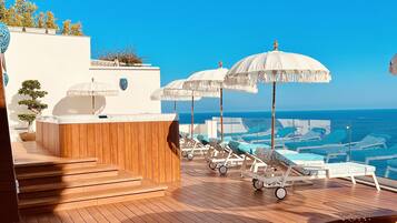 A wooden deck with hexagonal tiles, lounge chairs, and white umbrellas overlooking a body of water.