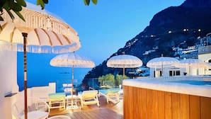 A wooden deck with outdoor seating, umbrellas, and a bar area overlooking a coastal landscape.