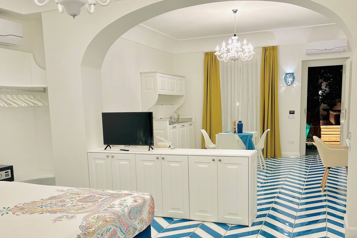 Ein Hotelzimmer mit Bett, Schreibtisch, Fernseher, weißen Schränken, einer Chandelüster und einem gemusterten Boden.