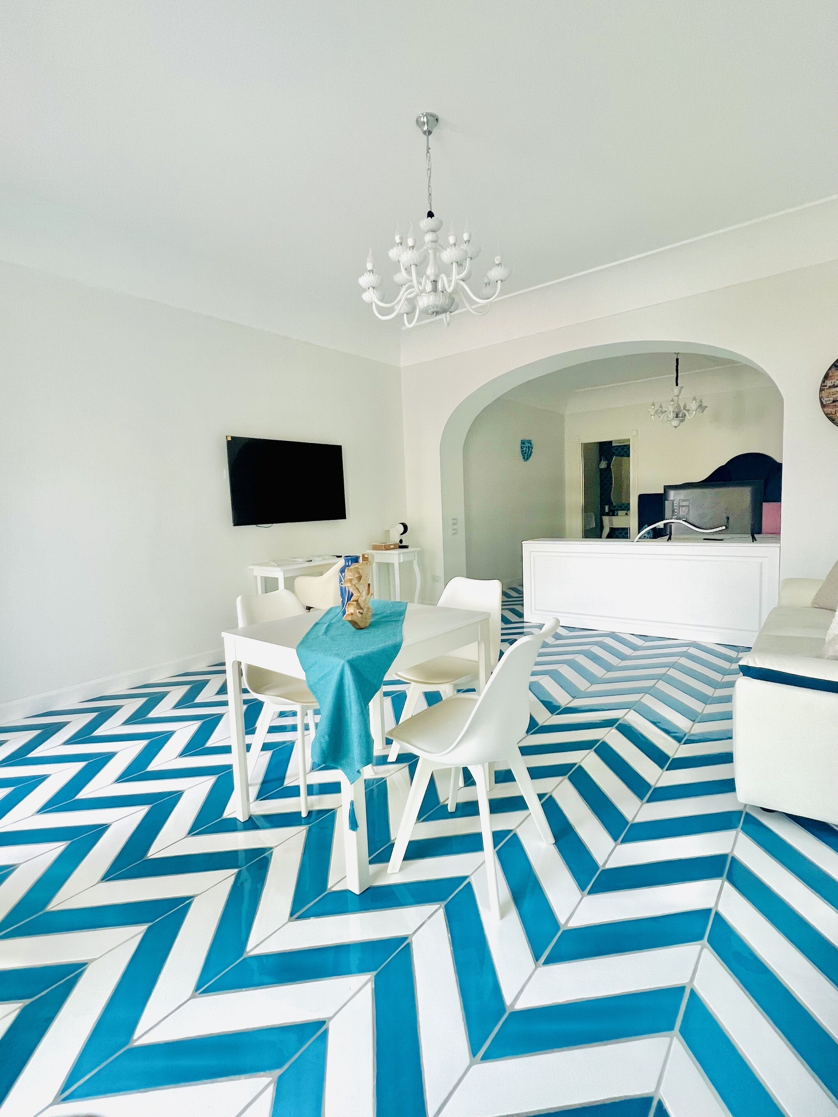 A modern living room with a blue and white chevron-patterned floor, white furniture, and a chandelier.