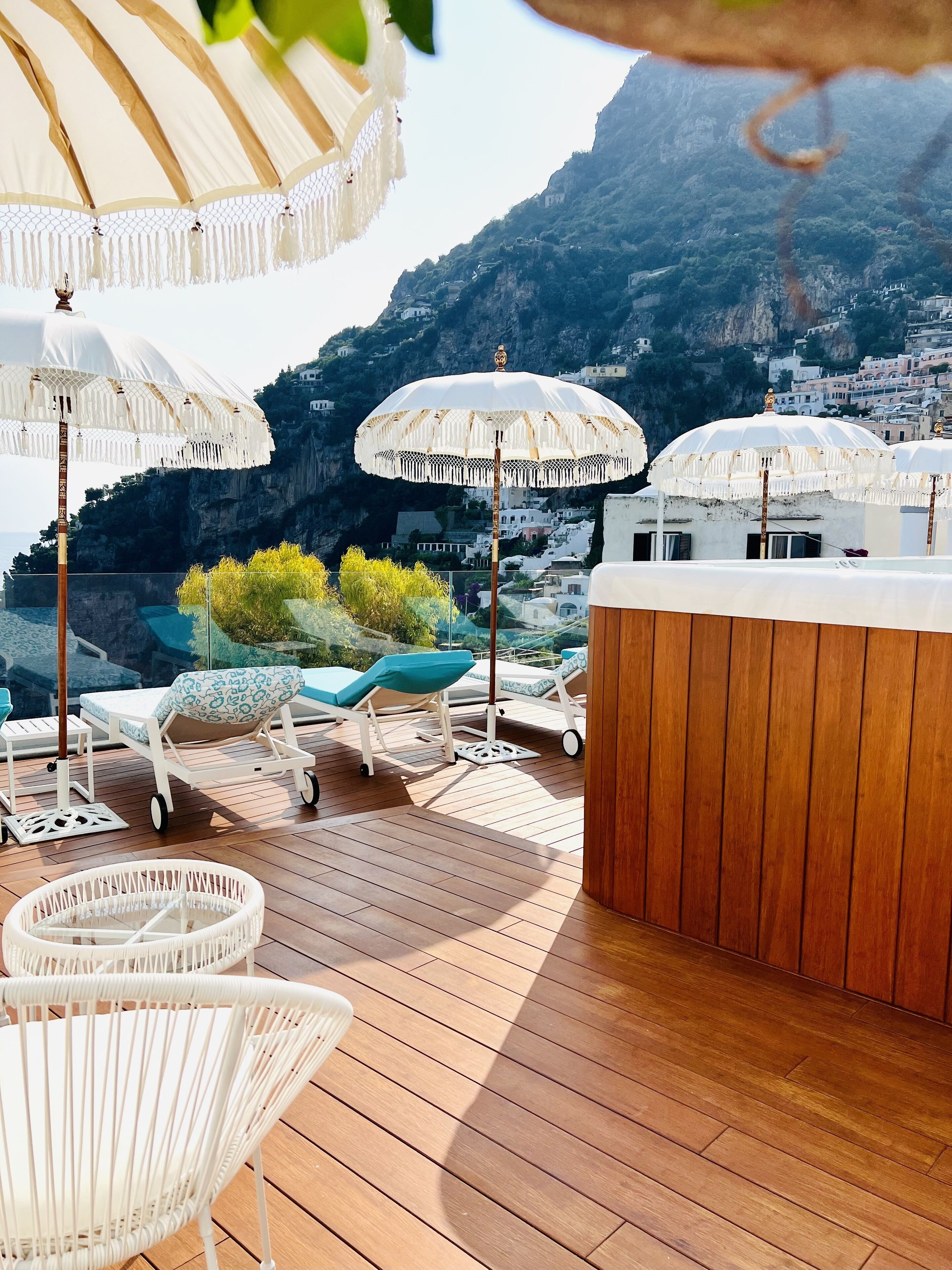 A rooftop terrace with wooden flooring, white lounge chairs, and white umbrellas.
