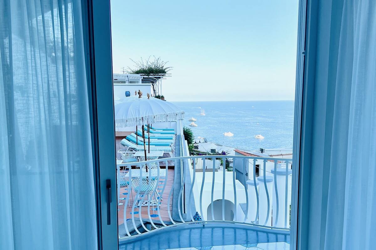 Ein Balkon mit Blick auf das Meer, weiße Vorhänge und ein Fliesenboden.