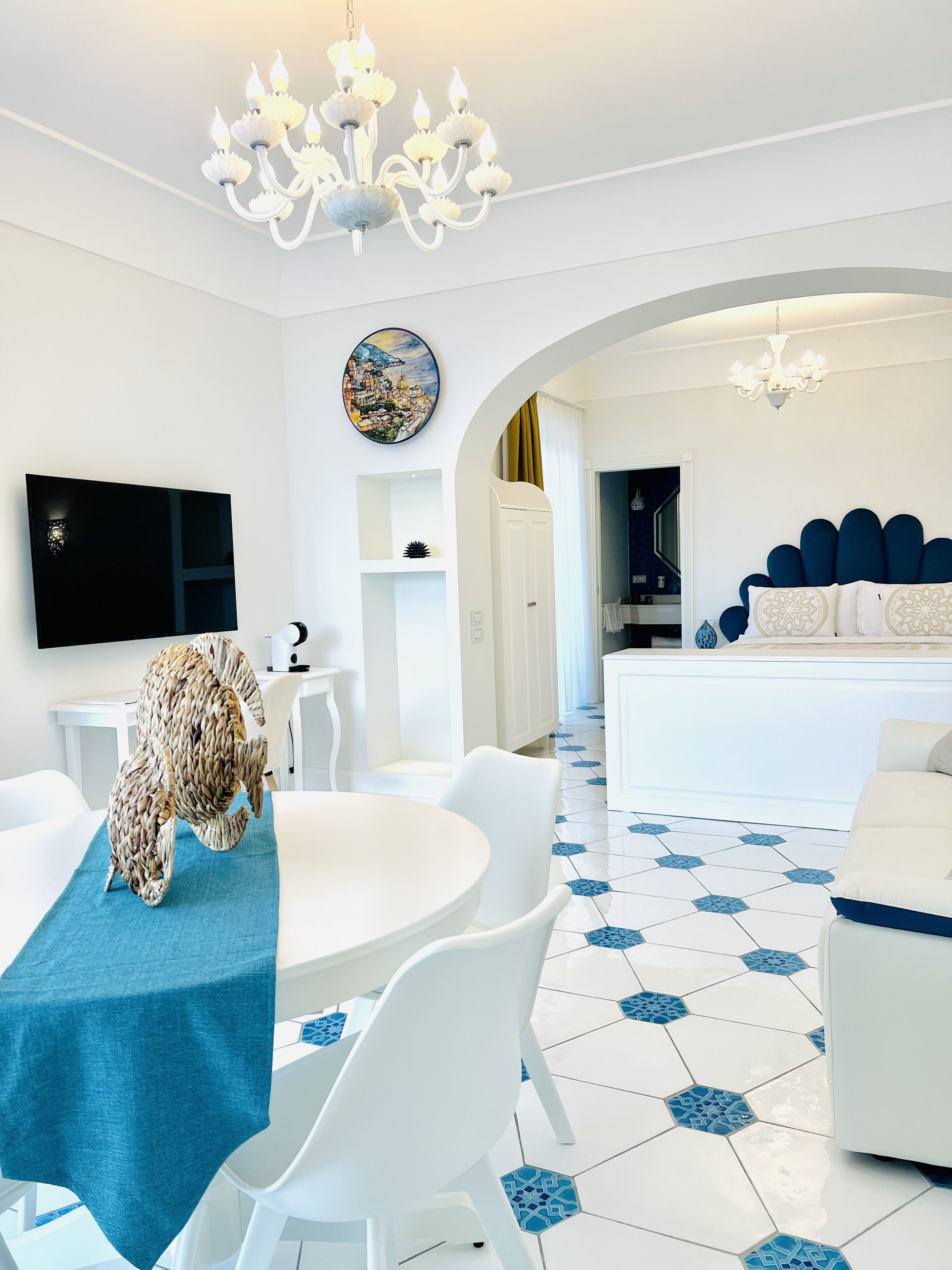 Ein modernes Wohnzimmer mit einem runden Esstisch, weißen Stühlen, einer Chandelier und einem großen Bett mit blauer Kopfteil.