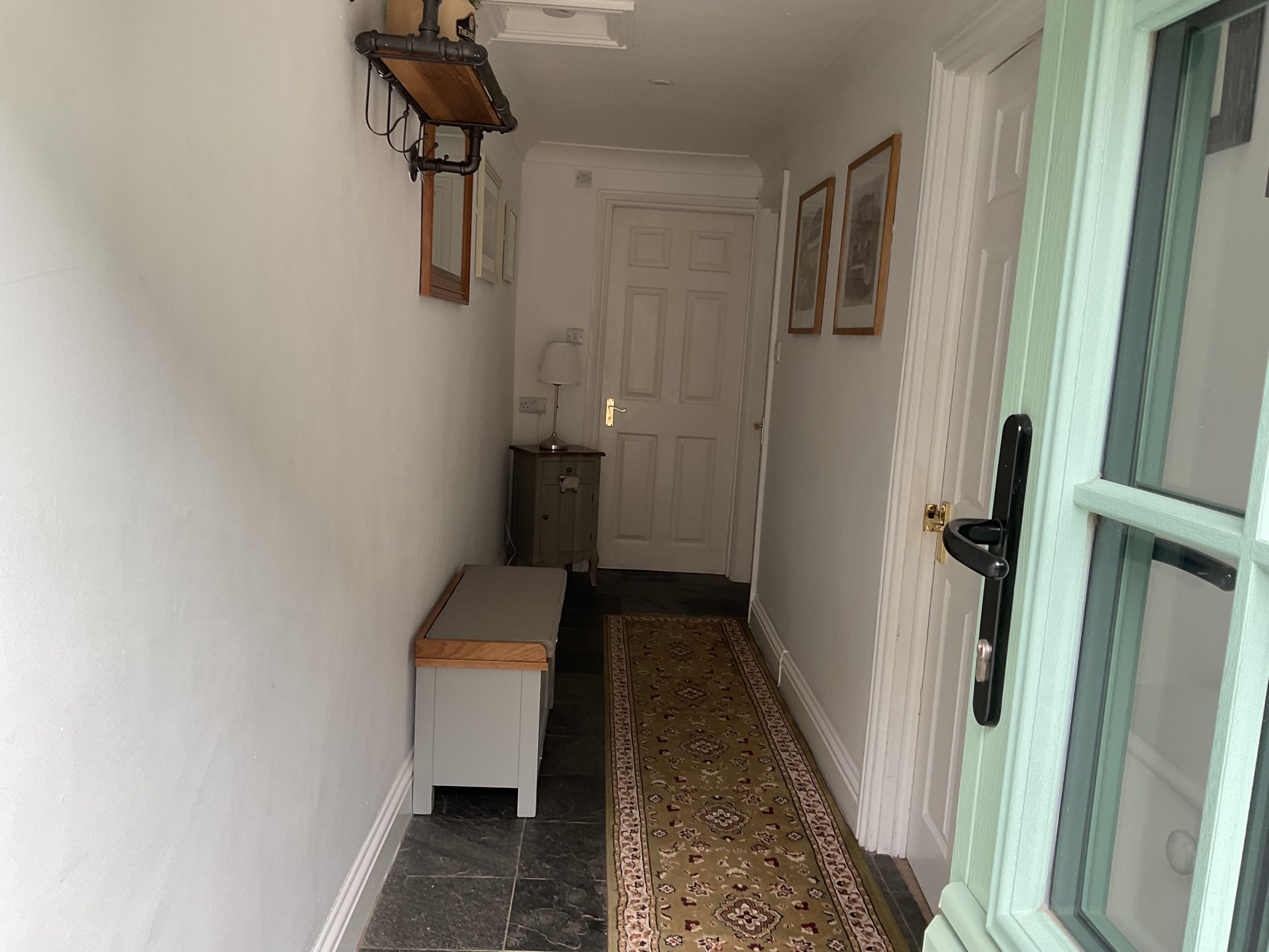 A narrow hallway with a bench, a door, and a patterned rug.