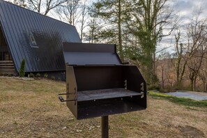 A barbecue grill with a flat grate, positioned outdoors with a house and trees in the background.