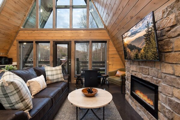 Un interior acogedor con chimenea, techo de madera y un ventanal que da a un bosque.