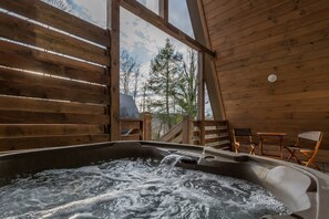 A wooden cabin interior with a hot tub, wooden walls, and a view of trees and mountains.