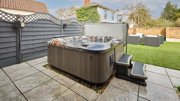 A hot tub in a backyard with a tiled patio, a wooden fence, and a house in the background. - Host & Stay | Casa Feliz (Skirlaugh)