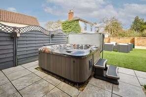 A hot tub in a backyard with a tiled patio, a wooden fence, and a house in the background. - Host & Stay | Casa Feliz (Skirlaugh)