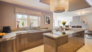 A modern kitchen with a central island, a dining area with a long table, and a hanging light fixture. - Host & Stay | Casa Feliz (Skirlaugh)