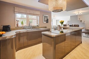 A modern kitchen with a central island, a dining area with a long table, and a hanging light fixture. - Host & Stay | Casa Feliz (Skirlaugh)