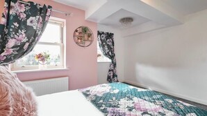 A bedroom with a bed, floral curtains, a window with a view, and a ceiling light fixture. - Host & Stay | Casa Feliz (Skirlaugh)