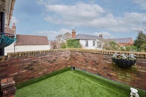A fenced backyard with a grassy area, brick wall, and a flower pot. - Host & Stay | Casa Feliz (Skirlaugh)