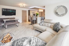A modern living room with a sofa, a dining area, and a kitchen in the background. - Host & Stay | Casa Feliz (Skirlaugh)