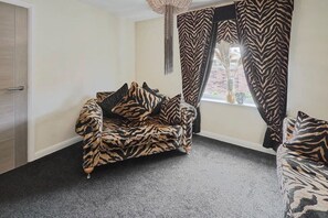 A room with a zebra-patterned sofa, a window with zebra-patterned curtains, and a door. - Host & Stay | Casa Feliz (Skirlaugh)