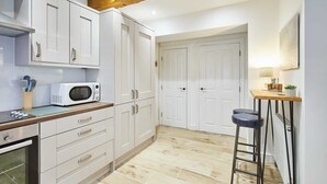 Une cuisine avec des armoires blanches, un four à micro-ondes, un plan de travail en bois et un tabouret.
