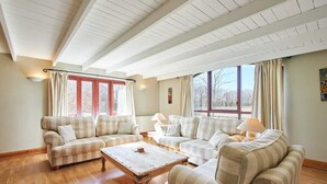 A cozy living room with a wooden coffee table, two sofas, and large windows with curtains. - Host & Stay | The Coach House (Beal)