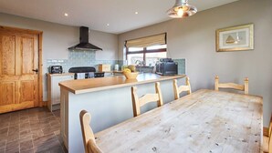 A modern kitchen with a wooden dining table, a large island, and a view of the outdoors. - Host & Stay | The Coach House (Beal)